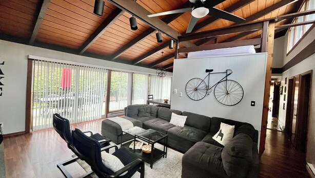 A spacious living room with a high ceiling and wooden beams, a large sofa set, a coffee table, and a bicycle wall art piece.