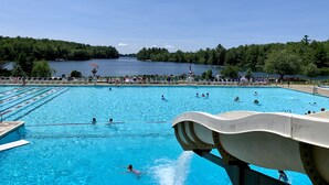 Ein Schwimmbad mit klarem, blauem Wasser, umgeben von Bäumen und Blick auf einen See.
