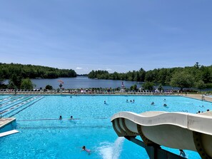 A swimming pool with clear blue water, surrounded by trees and a view of a lake.