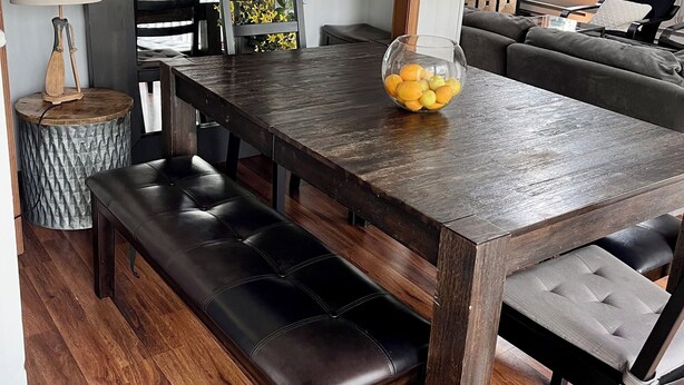 Un comedor con una mesa de madera oscura, bancos acolchados negros y un cuenco de vidrio con fruta.