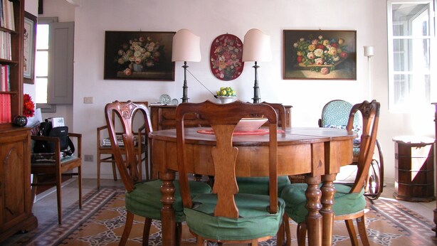 A dining room with a wooden table surrounded by chairs, two wall-mounted lamps, and floral paintings. - Attic with views in Piazza Santa Croce (Firenze)