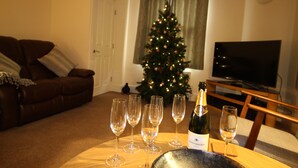 Ein Wohnzimmer mit Weihnachtsbaum, einer Couch, einem Fernseher und mehreren Weingläsern auf einem Tisch.