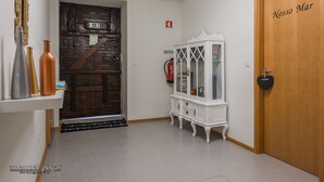A hallway with a wooden door labeled "Nossos Mar," a white cabinet with glass doors, and a chandelier. - Apartment with Patio Centro de Ovar (Ovar)