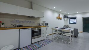A modern kitchen with white cabinets, a microwave, and a built-in oven. There is a dining area with a table and chairs, and a colorful rug on the floor. - Apartment with Patio Centro de Ovar (Ovar)