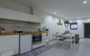 A modern kitchen with white cabinets, a microwave, and a built-in oven. There is a dining area with a table and chairs, and a colorful rug on the floor. - Apartment with Patio Centro de Ovar (Ovar)
