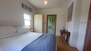 A bedroom with a bed, a bedside table, a lamp, a wardrobe, a small table with a decorative item, and a mirror.