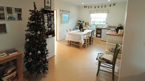 Una habitación acogedora y bien iluminada con un árbol de Navidad, una mesa de comedor con sillas, una zona de cocina y una pared decorada con marcos.
