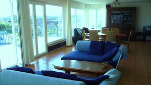 Ein Wohnzimmer mit einer Couch, Sesseln, einem Tisch und Blick durch große Fenster.