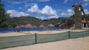 Ein Strand mit einem Netzstaketenzaun, Sonnenschirmen und einem Rettungsturm.