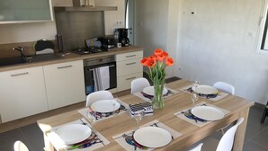 Une cuisine moderne avec des meubles blancs, un plan de travail en bois et un coin repas comprenant une table en bois dressée pour quatre personnes.