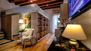 Una sala de estar acogedora con piso de madera, un sofá, un sillón, una estantería y un televisor en la pared.