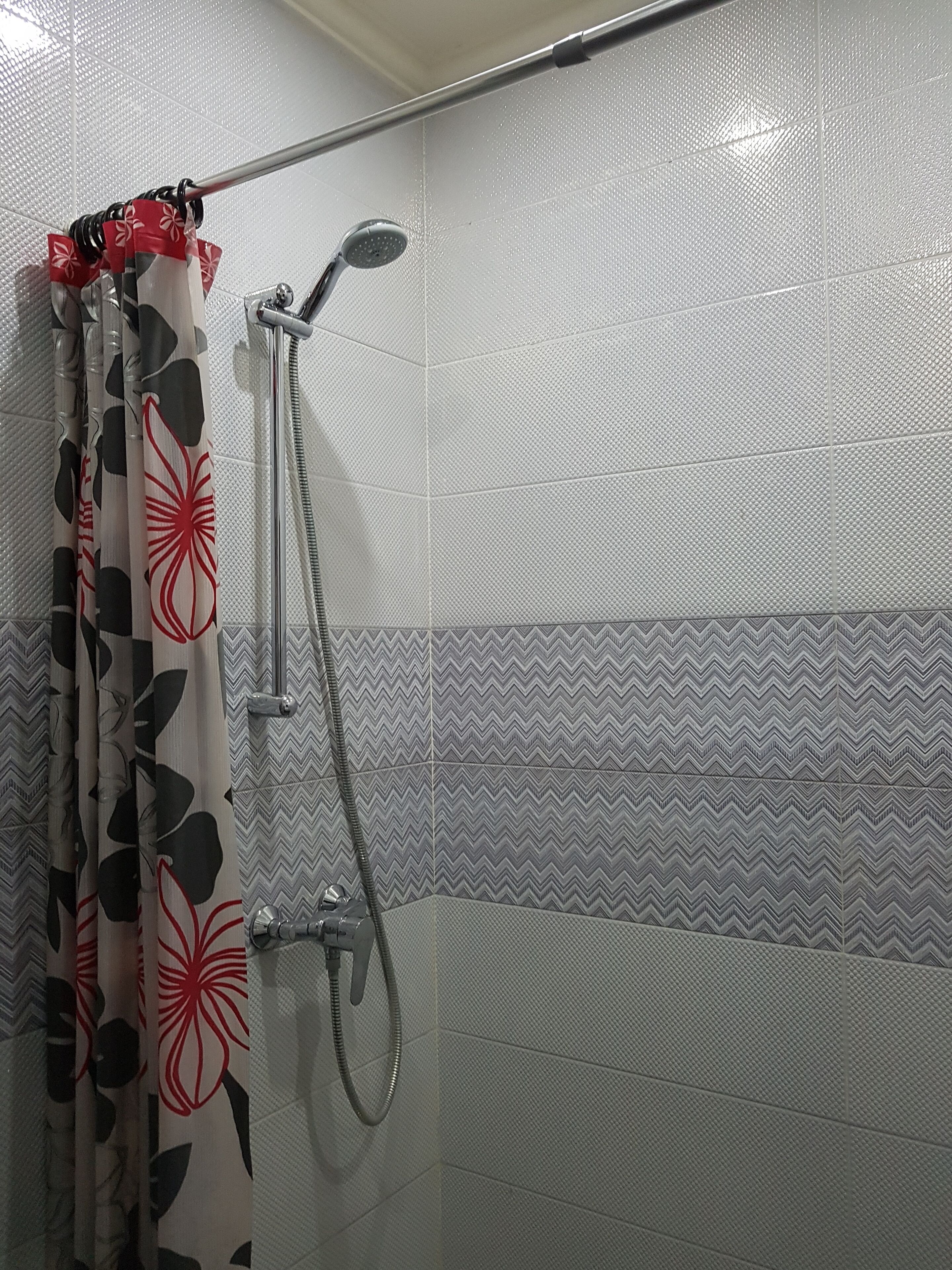 Ein Duschbereich mit Regendusche, Handbrause und einer Duschvorhang mit Blumenmuster.