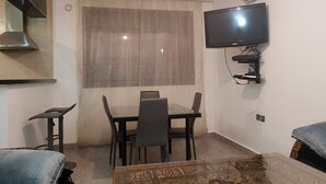A compact living space with a dining table, chairs, a sofa, a coffee table, and a mounted TV. - 3 modern new rooms with satelite wifi and air conditioning (agadir)