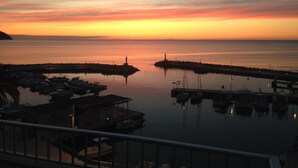 A marina at sunset with boats docked, a pier, and a lighthouse in the distance. - Arrive near the beach & feel good. (Sant Llorenç des Cardassar)