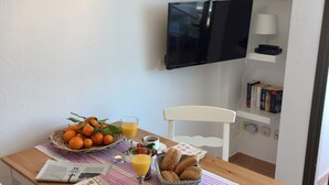 A dining area with a wooden table, chairs, a basket of oranges, a basket of bread, a glass of orange juice, and a candle. - Arrive near the beach & feel good. (Sant Llorenç des Cardassar)
