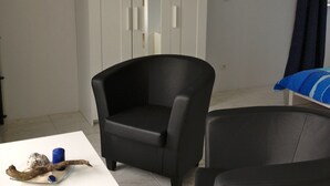 A room with a white wardrobe, a black armchair, a small table with decorative items, and a bed with a blue and white striped blanket. - Beautiful, natural flat with big terrace in the heart of the island of Rügen (Patzig)