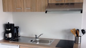 A modern kitchen with wooden cabinets, a stainless steel sink, a coffee maker, and a utensil holder. - Beautiful, natural flat with big terrace in the heart of the island of Rügen (Patzig)