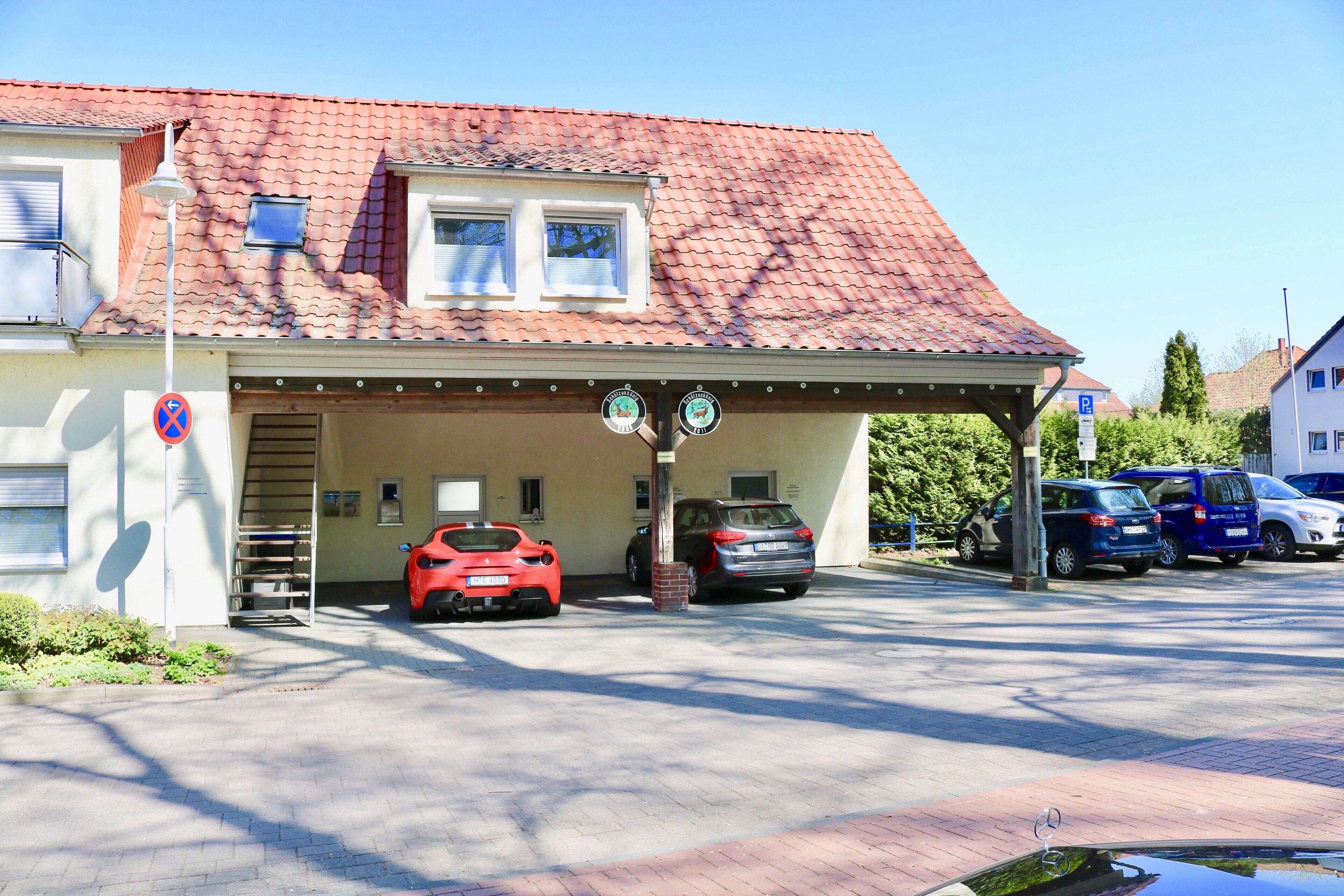 Ein Gebäude mit roten Ziegeldach, einem überdachten Parkbereich und einem roten Sportwagen davor.