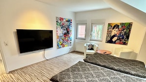 A modern bedroom with a large bed, a flat-screen TV, and artwork on the walls. - Comf. mod. Apartment -Anker-(120m2) in the middle of Steinhude, wallbox, parking lot, WLAN, (Wunstorf)