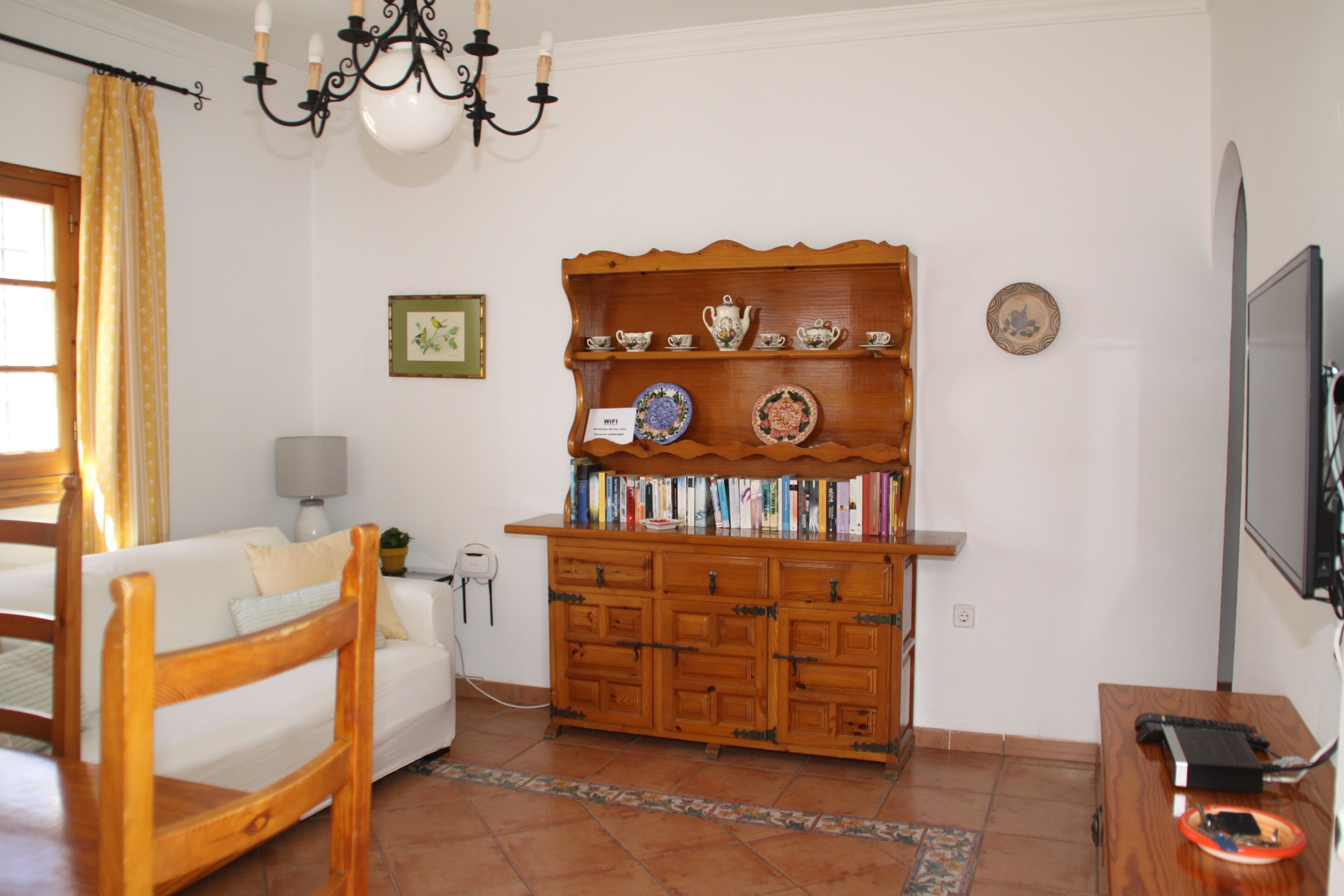 Un salon avec un meuble en bois, un canapé blanc, une chaise en bois, un téléviseur et une lampe.