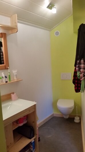 Une petite salle de bain comprenant des toilettes, une étagère avec des articles de toilette et un meuble en bois.