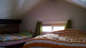 Une chambre de dortoir avec deux lits, une fenêtre avec des rideaux et un plafond en pente.