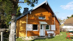Une maison en bois à deux étages, avec une porte d’entrée, un petit porche et un banc.