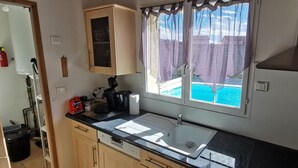 Une cuisine équipée d’un évier, d’une cuisinière et d’une fenêtre donnant sur une piscine.