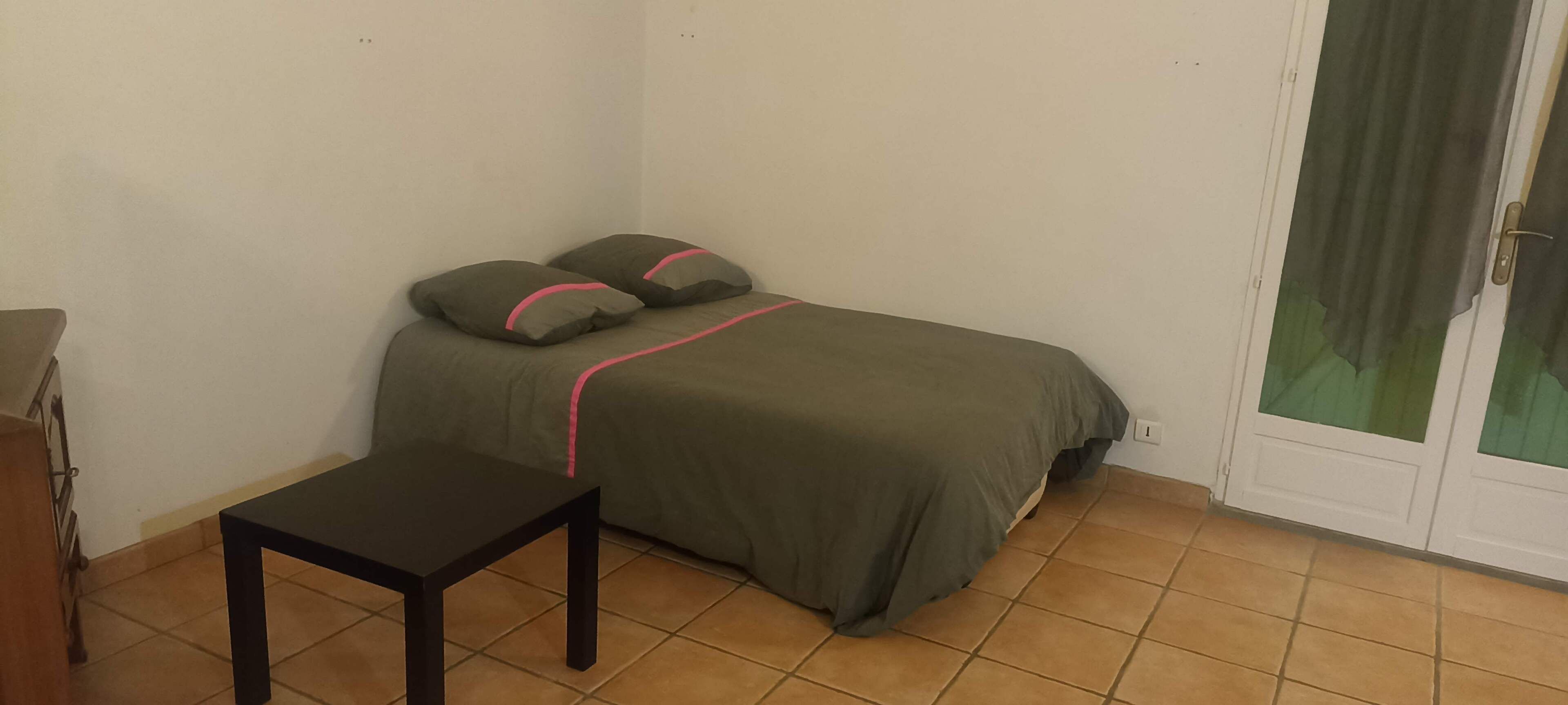 A small room with a bed, a table, and a door with a curtain.