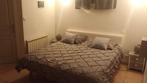 Une chambre à coucher comprenant un lit, une table de chevet, une lampe fixée au mur, un radiateur et une porte.