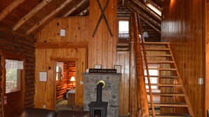 A log cabin interior with a stone fireplace, wooden staircase, and a leather sofa. - Stay WATERFRONT !   Stay CHEAT RIVER LODGE (Elkins)