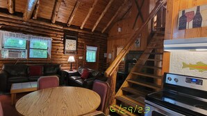 A cozy cabin-style interior with a wooden interior, a dining area with a round table, a kitchen with a stove, and a staircase. - Stay WATERFRONT !   Stay CHEAT RIVER LODGE (Elkins)