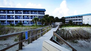 A wooden boardwalk leading to a beachfront hotel with multiple balconies and a sandy beach. - “TYBEE ISLAND DREAMING”Private Balcony Overlooking the Ocean, Beautiful View.  (Tybee Island)