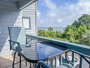 A balcony with a glass table and chairs, overlooking a view of the ocean and lush greenery. - “TYBEE ISLAND DREAMING”Private Balcony Overlooking the Ocean, Beautiful View.  (Tybee Island)