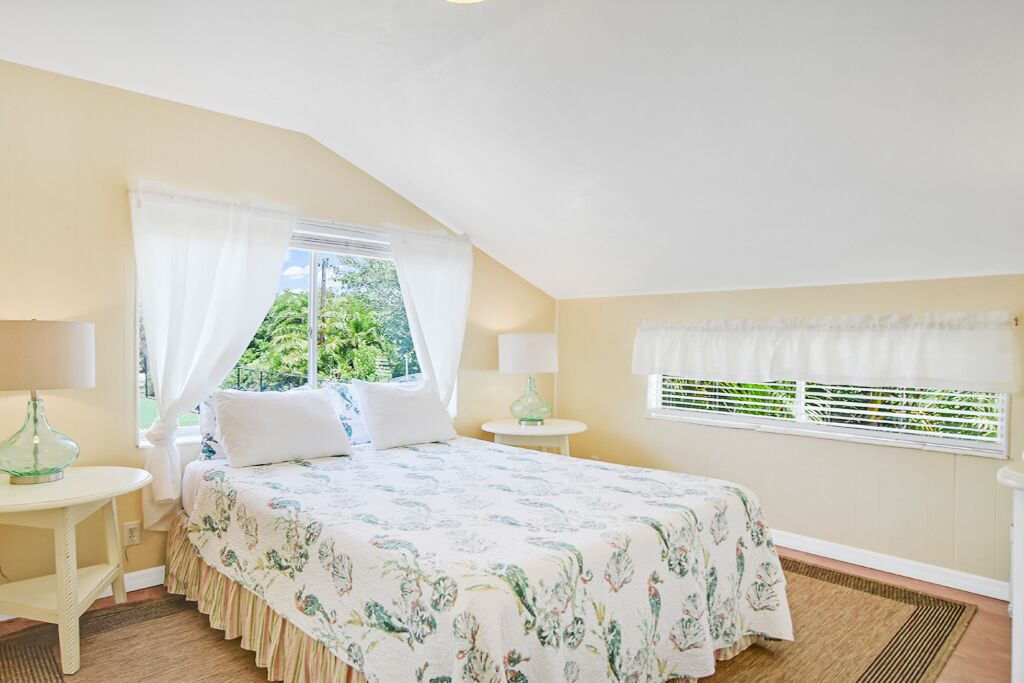 Una camera da letto con un letto, due comodini, una finestra con tende e vista sul verde.