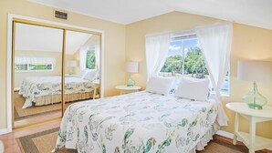 Une chambre à coucher avec un lit, un miroir, une fenêtre avec des rideaux et une petite table avec une lampe.