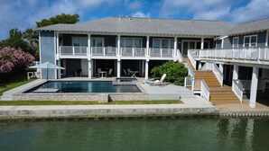 Ein großes, zweistöckiges Haus mit Swimmingpool, Sitzgelegenheiten im Freien und einer Treppe, die zu einem Balkon führt.