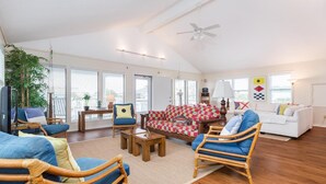 Ein geräumiges Wohnzimmer mit hoher Decke, großen Fenstern und einem Deckenventilator.