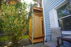 A wooden outdoor storage shed with a door, a chair, and a table nearby.