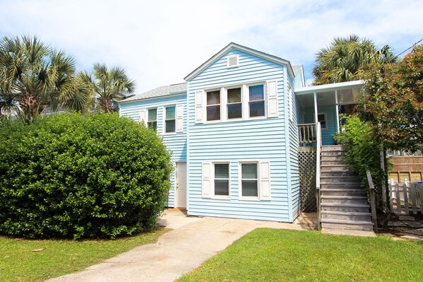 A two-story house with a front porch, a small front yard, and a wooden staircase leading to a covered porch. - 2 Blocks to Beach • Dog-Friendly 2BR • Private Downstairs Retreat • Fenced Yard (Isle of Palms)