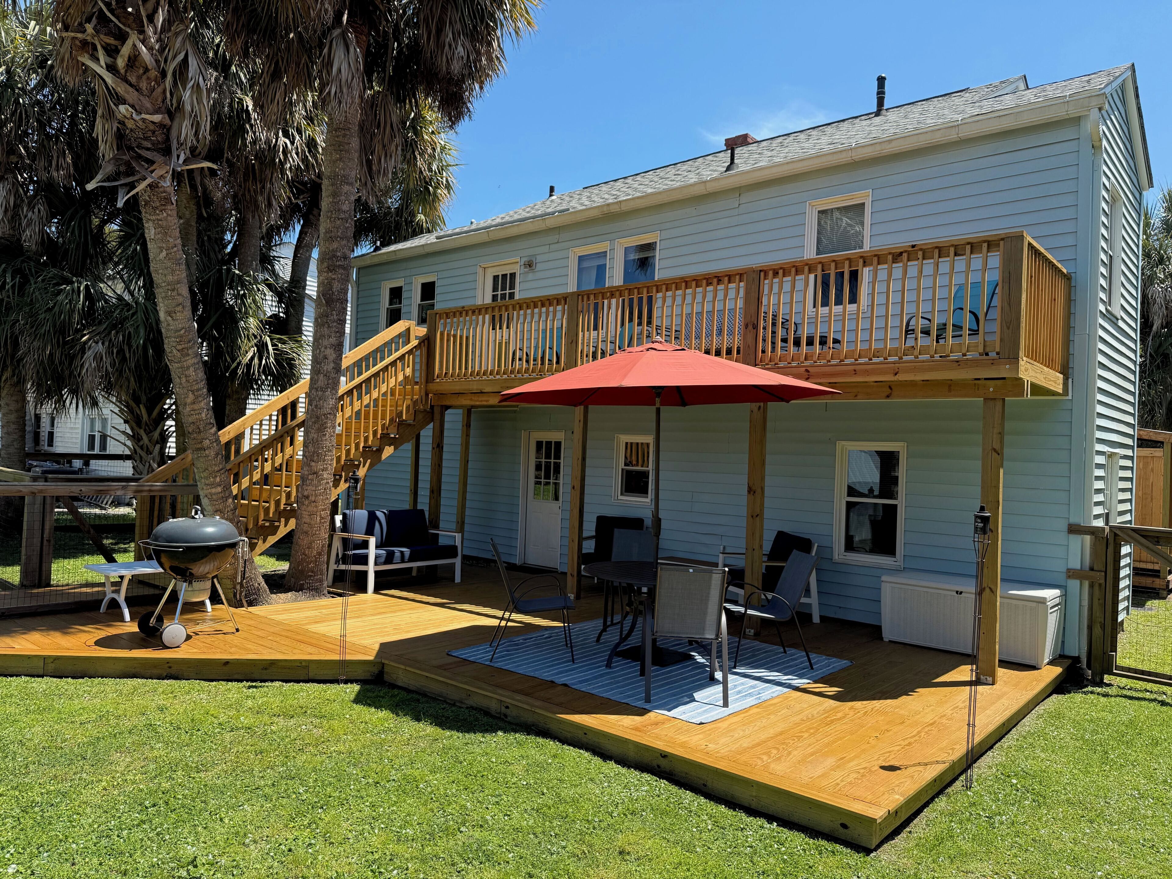 Une maison à deux étages avec une terrasse en bois, du mobilier d’extérieur et un parasol rouge.