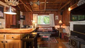 L’intérieur d’un chalet rustique est aménagé avec une table à manger en bois, un canapé en cuir, une cheminée et un téléviseur.