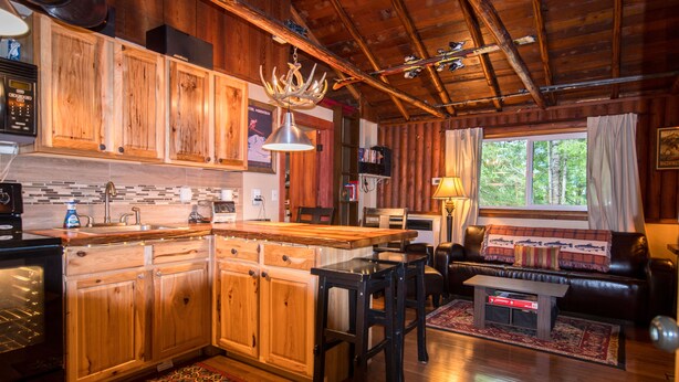 L’intérieur d’un chalet rustique est agrémenté de meubles en bois, d’un coin cuisine, d’un espace repas et d’un salon avec un canapé en cuir et une cheminée.