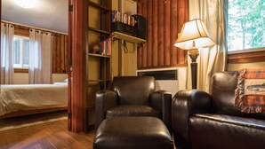 Une pièce comprenant un lit, des fauteuils en cuir, une bibliothèque, une lampe et une fenêtre avec des rideaux.