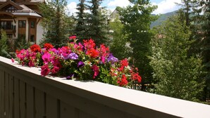 Un balcon orné de nombreuses fleurs aux couleurs vives, une balustrade en bois et, au fond, une maison avec un toit en pente.
