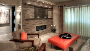 Un salon moderne avec un mur en pierre, un téléviseur à écran plat et un pouf rouge.