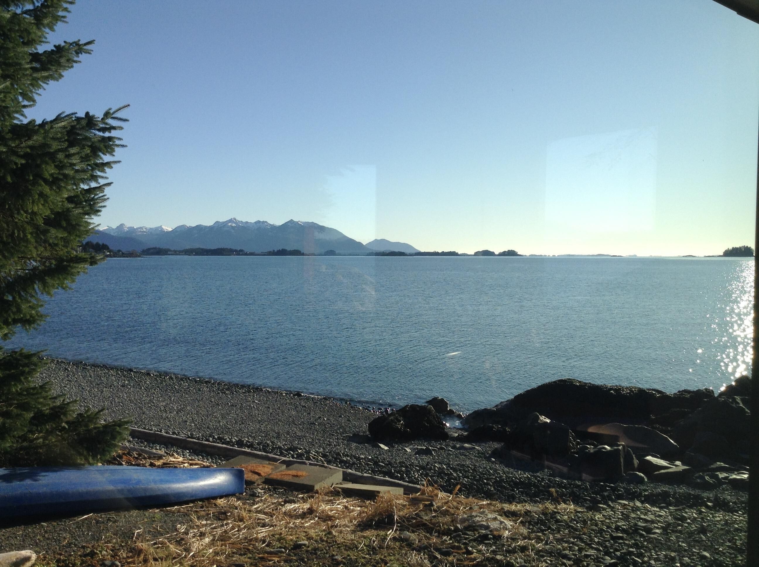 A lakeside view with mountains in the background, a rocky shoreline, and a clear sky.