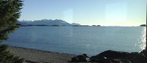 A lakeside view with mountains in the background, a rocky shoreline, and a clear sky.