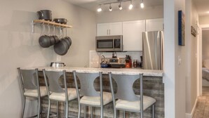 A modern kitchen with a bar area, stainless steel appliances, and a hanging pot rack. - Slope-Side 1 Bedroom, Walk to Chairlifts! (Big Sky)