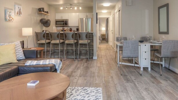 A modern living room with a sofa, a coffee table, and a dining area with a table and chairs. - Slope-Side 1 Bedroom, Walk to Chairlifts! (Big Sky)